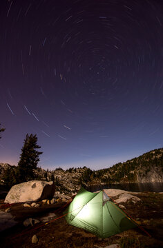 View of star trail over illuminated tent by Robbins Lake at night