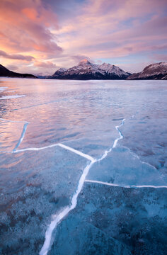 Sunrise over Elliot Peak and cracks in frozen Abraham Lake in Alberta, Canada