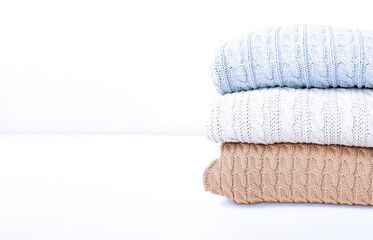 Stack of cozy comfortable homely clean washed knitted sweaters in pastel colors, laundry and washing clothes concept, copy space