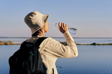 A person drinks water by a tranquil lake, enjoying a peaceful moment in nature.