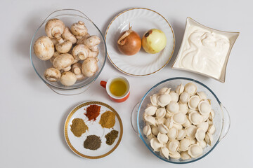 Mushrooms and onions with sour cream, raw dumplings in a transparent bowl on the kitchen table.