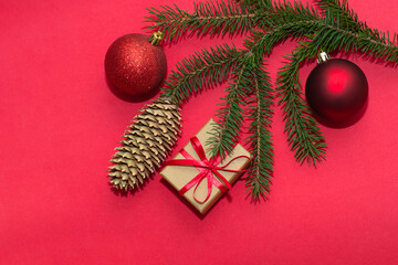 Natural spruce tree branch with a fir cone and Christmas decorations on a red background. Merry christmas and New Year. A minimalist composition, celebration and giving gifts. Copy space, flat lay.