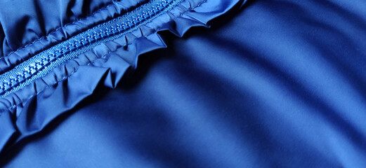 Buttoned zip on a blue raincoat. Waves and folds in the fabric. Beautiful flounces, ruffles,...