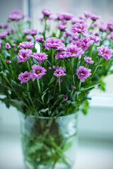 A bouquet of purple chrysanthemums in a glass vase on the table. To close. Selective focus.