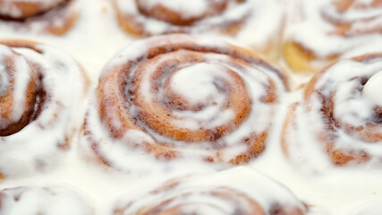 Freshly baked cinnamon rolls with frosting close up, top view. Sweet cream cheese frosting on cinnamon buns. Appetizing cinnamon bun