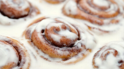Freshly baked cinnamon rolls with frosting close up, top view. Sweet cream cheese frosting on cinnamon buns. Appetizing cinnamon bun