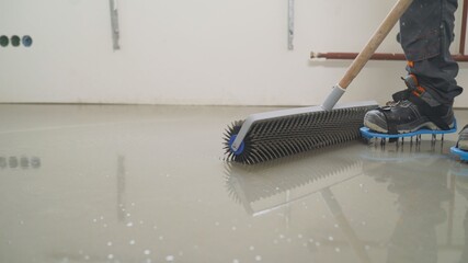 Leveling the screed with a roller. Interior of apartment under construction. Roller application....