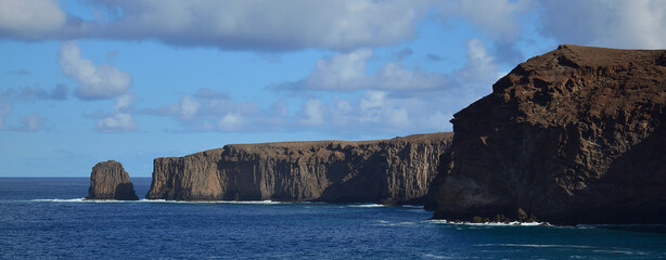 Panoramic image of rocky coast with cliffs, calm sea and blue sky with clouds, north of Gran Canaria, Spain