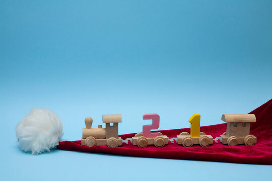 The children's train carries the number 21. The train on a blue background. A children's steam locomotive stands on the hat of Santa Claus. Christmas decorations around the locomotive. Coming 2021