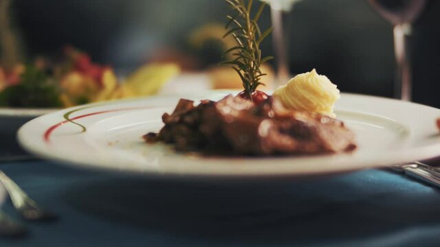 Close-up shot of the food served on the plate on the dining table. 
waiter serving dish. Close up shot of waiter  hand putting a plate with steak. luxury restaurant.4K.