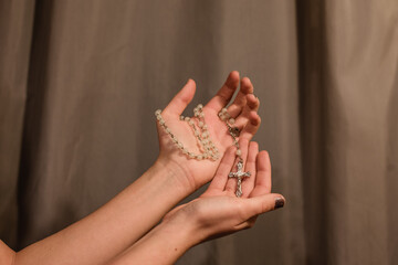 Unas manos sujetando un rosario blanco sobre fondo gris