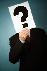 Businessman holding a sign with a question mark in front of face.