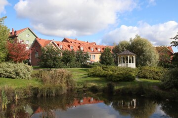 A view to a public park with a gazebo and a small pond. Behind the park, there are colorful residential buildings. These modern buildings are built on a traditional way. Scandinavian architecture.