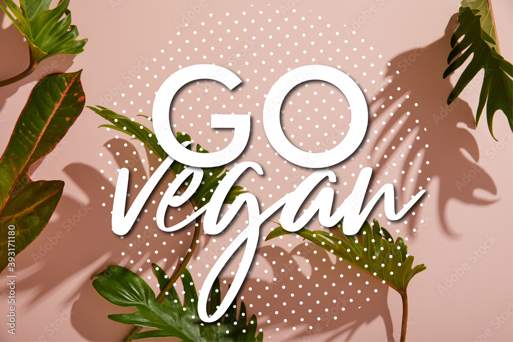 Wall mural fresh tropical green leaves on pink background with go vegan illustration