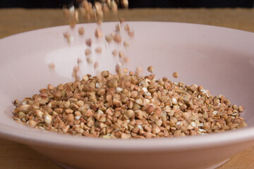 Buckwheat grains pour into plate on the table of the oz tree