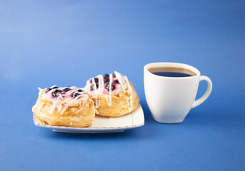 White ceramic cup of hot coffee and sweet pastries on blue background