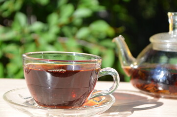 A girl pours tea from a transparent teapot into a transparent cup against a background of green foliage Good morning, outdoor cafe, energy boost. Tea being poured into glass tea