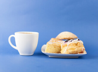 White ceramic cup of hot coffee and sweet pastries on blue background