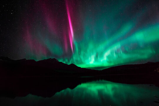 Northern lights dancing in the sky, reflecting in a lake. Aurora Borealis shot in Jasper National Park, Canada. 