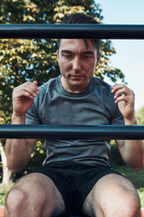 Young man doing sit-ups during his workout in a modern calisthenics street workout park. Man sitting on a sit-up board wearing sportswear