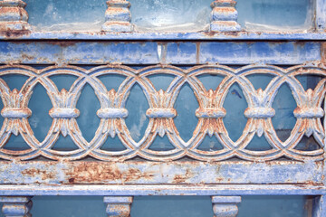 An iron ornament on an old building, rusty with peeling blue paint.