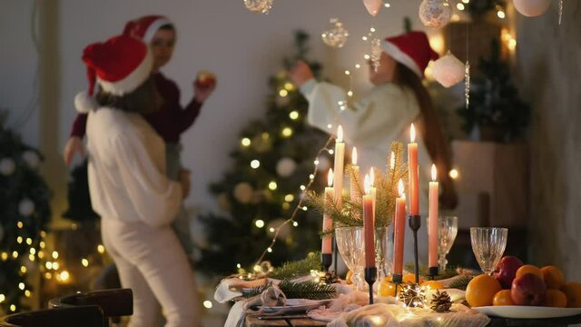 Christmas table with candles in focus on the background of a dancing and singing family of three. Merry Christmas and Happy New Year