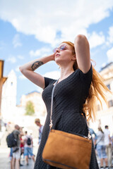 Ginger woman in dress putting tidy her hair in sunny day with blue sky