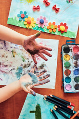 Little girl preschooler showing painted colourful hands. Child having fun making a stamps on sheet of paper with painted hands during an art class in the classroom