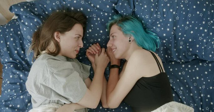 Two LGBT lesbian girls lying on the bed at home in the morning facing each other in love looking into the eyes of a loved one and talking smiling