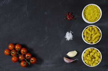 Different Italian dry Pasta fusilli, capellini, macaroni,  on the dark background with garlic, tomatoes, red pepper