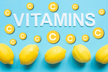 top view of ripe yellow lemons and word vitamins on blue background