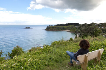 Man with curly hair looking at the ocean, sitted on bench, Waiheke Is.