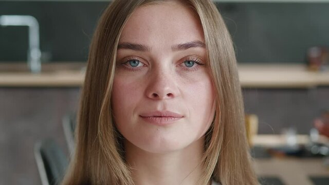 Close-up attractive young european woman model looking at camera at home. Portrait if beautiful female professional with pretty face and blue eyes stand alone indoors