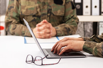Military officers meet to discuss recruitment. They are using a laptop.
