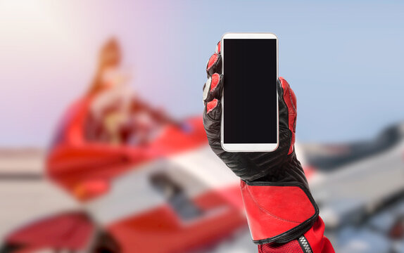 Biker hand holding smartphone with blank screen, cropped image, copy space, blank screen for graphic design with a motorcycle in the background
