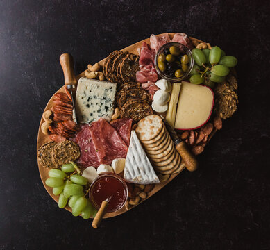 Top view of charcuterie board of meat and cheese on black surface.