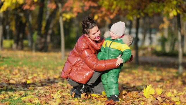 4k footage of little boy with mother collecting and picking golden autumn leaves at park slow motion shot.