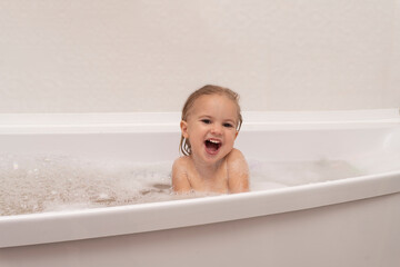 Cute caucasian naked kid plays with white foam at bathroom, laughts, happy childhood concept, white background, copy space.