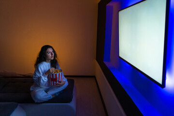 person watches a movie sitting on the couch with a bucket of popcorn