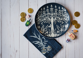 Decorative Hanukkah plate, dreidels and chocolate coins on white wood.