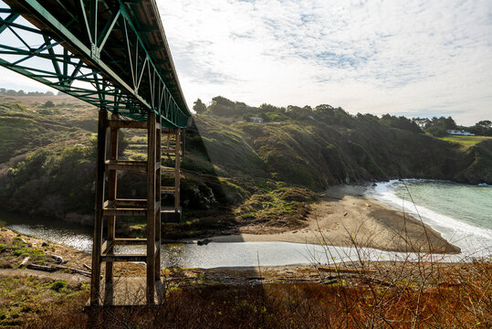 Low view of bridge above river leading to beach by cliffside houses