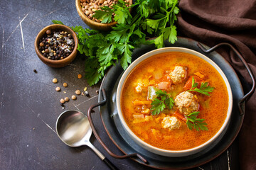 Tomato-lentil soup with meatballs and vegetables on a dark slate table top. Copy space.