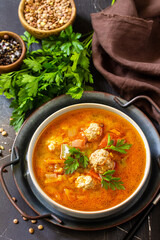 Tomato-lentil soup with meatballs and vegetables on a dark slate table top.