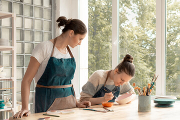 Woman making ceramic pottery. Attractive skilled young lady in apron standing at table and teaching student. Concept for workshop and master class