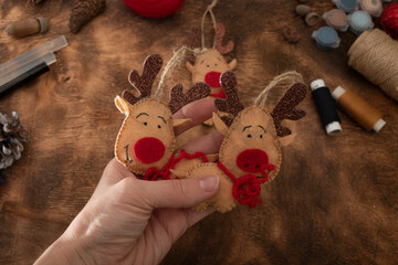 Holding a handmade Christmas tree toy. Felt toy - deer on wooden background. Ready for holidays.