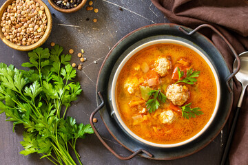 Tomato-lentil soup with meatballs and vegetables on a dark slate table top. Top view flat lay background.