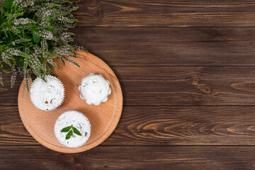 Cupcakes on a background of flowers and mint leaves, on a round board on a wooden background. Place for gadpis.