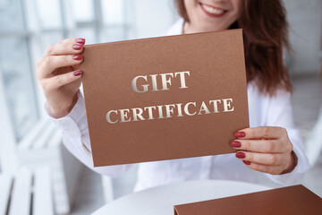 woman holding gift Certificate, gift voucher or discount. close-up photo of bronze invitation gift...