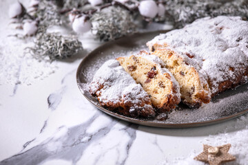 Traditional homemade german Christmas baking stollen cake bread on plate with silver xmas decorations over white marble background.