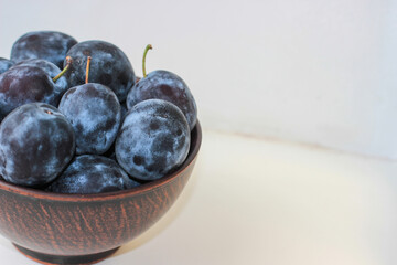 Several ripe blue plums in a deep clay plate on a white background with a copy space